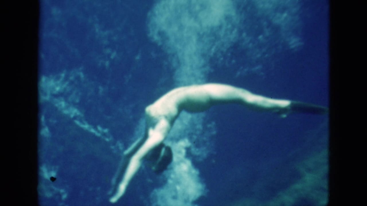 1952 Florida 8mm frame of a woman underwater, angled downward with swim fins as bubbles rise behind her in blue water.