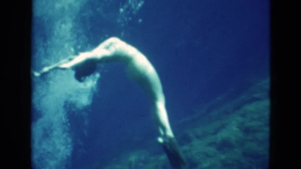1952 Florida 8mm frame of a woman underwater arcing backward beside a cloud of bubbles in blue water.