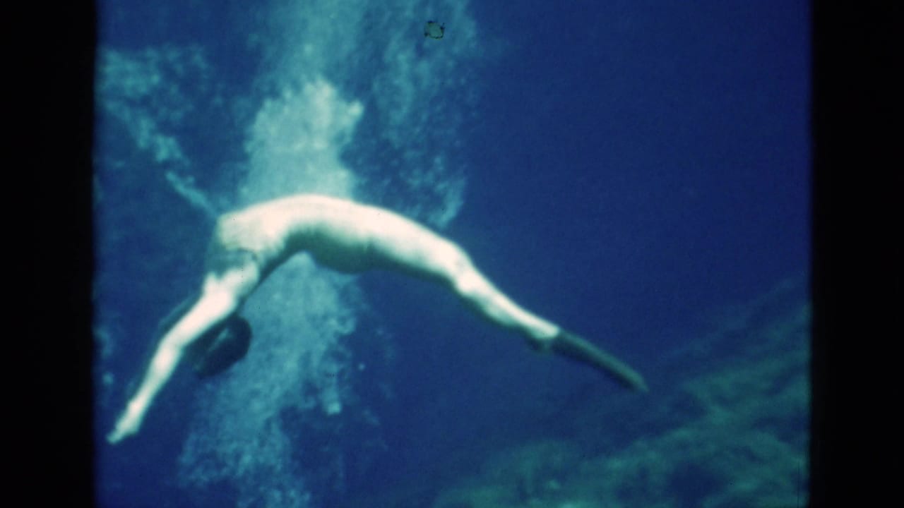 1952 Florida 8mm frame showing a woman underwater in a dark swimsuit, snorkeling mask, and fins as bubbles rise through blue water.
