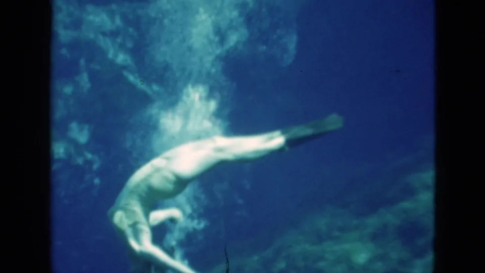 1952 Florida 8mm frame of a woman in mask and fins moving horizontally through deep blue water with bubbles above her.