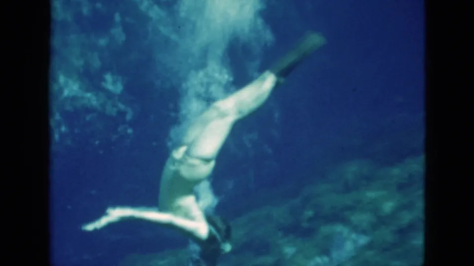 1952 Florida 8mm frame showing the swimmer rotating underwater, with fins above and bubbles diffusing through blue-green water.