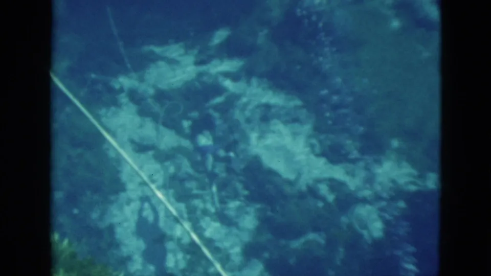 1952 Florida 8mm frame with soft blue underwater rocks, suspended particles, and a diagonal pale line through the scene.