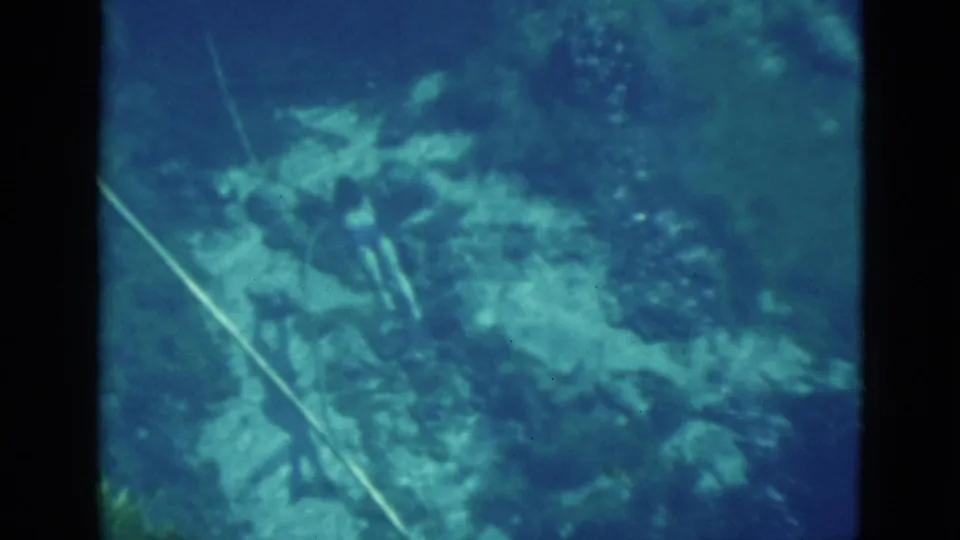 1952 Florida 8mm frame showing blue-green underwater rocks, a diagonal pale line, and soft vintage film texture.