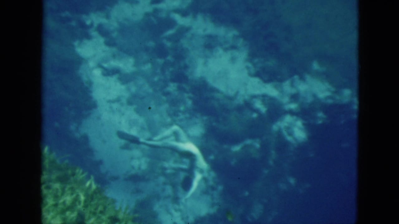 1952 Florida 8mm frame with a distant female diver crossing a blue underwater scene near reef formations.
