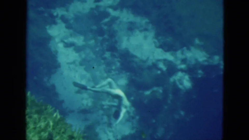 1952 Florida 8mm frame with a distant female diver crossing a blue underwater scene near reef formations.