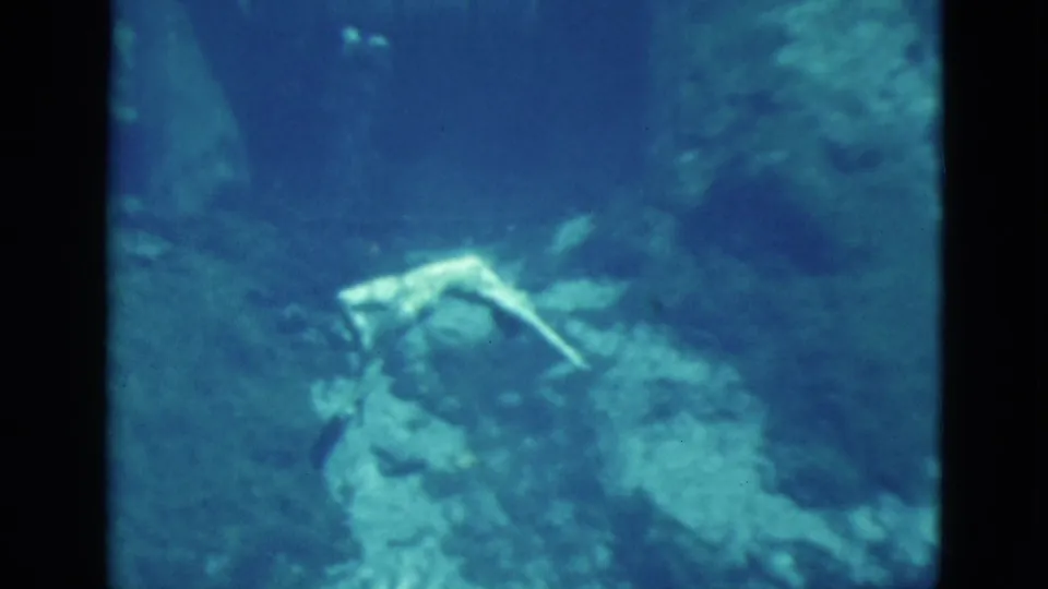 1952 Florida 8mm frame showing a woman swimming underwater over uneven rock in blue-green water.