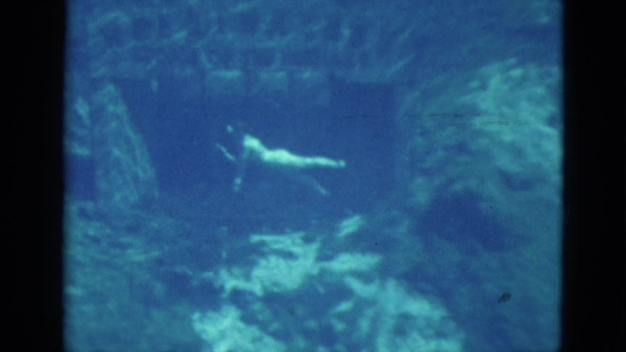 1952 Florida underwater home-movie frame with a woman gliding horizontally near rocky walls.