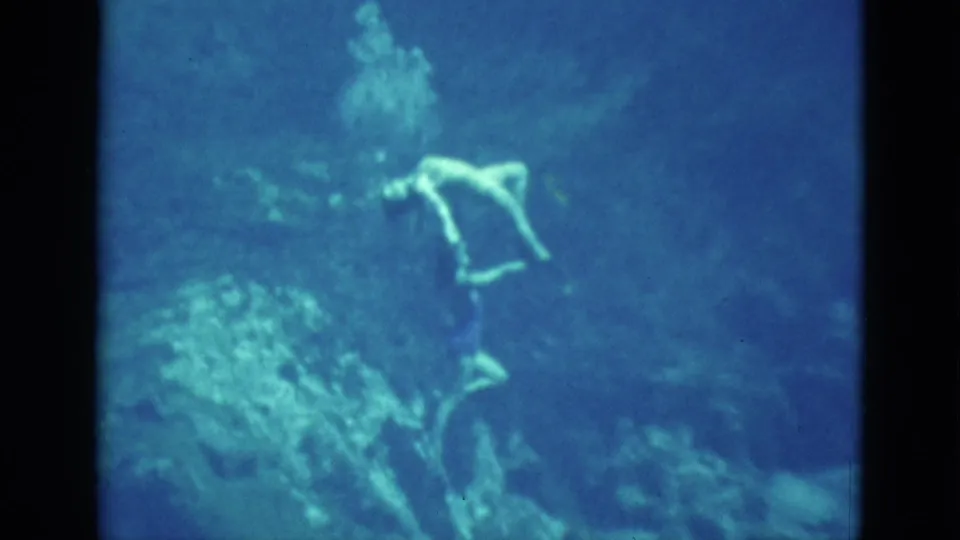 1952 Florida 8mm frame of a young woman underwater, softly focused as she holds a graceful pose in blue-green water.