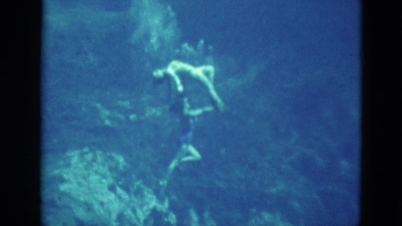 1952 Florida 8mm frame showing a swimmer suspended underwater, her pale outline visible against blue water and soft shadows.