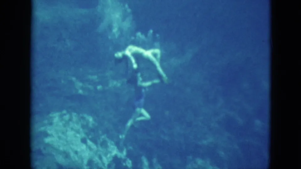 1952 Florida 8mm frame showing a swimmer suspended underwater, her pale outline visible against blue water and soft shadows.