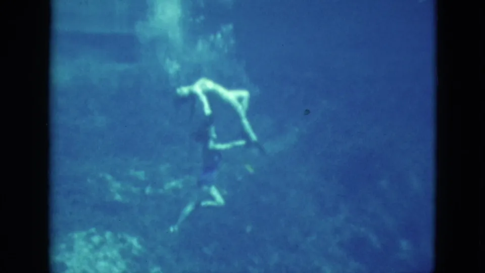 1952 Florida 8mm frame of a swimmer making an artistic underwater pose, softened by grain and blue color shift.