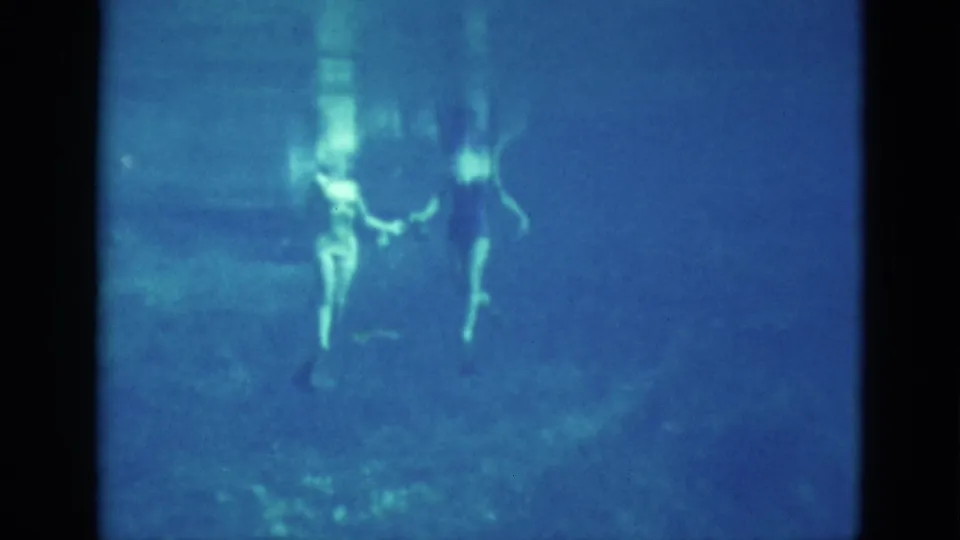 The swimmers are seen from below during the underwater routine, with legs, arms, bubbles, and soft pool reflections visible in the 1952 Florida home-movie frame.