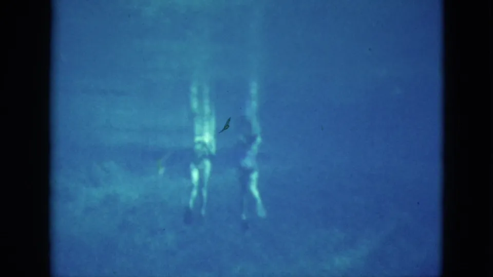 Two young women appear to turn or descend underwater near the end of the clip, partly obscured by the pool water and the soft 8mm image quality.