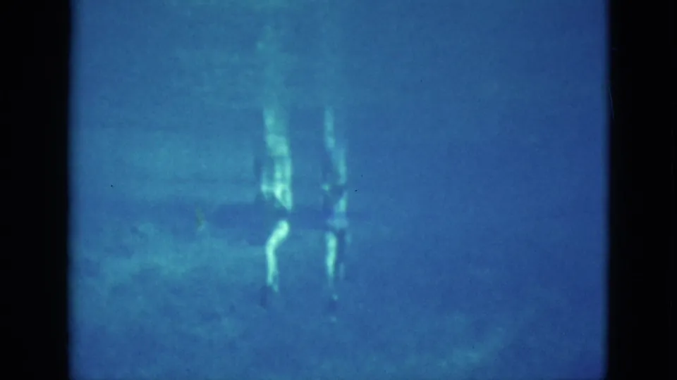 1952 Florida 8mm frame showing faint swimmers underwater in blue lake water with reflected light near the surface.