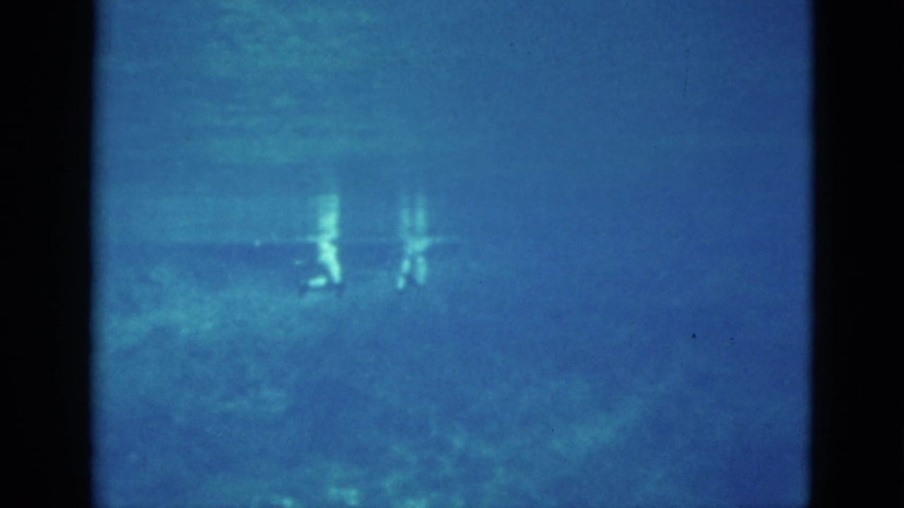 Blue underwater view with small reflected shapes and faint swimmers.