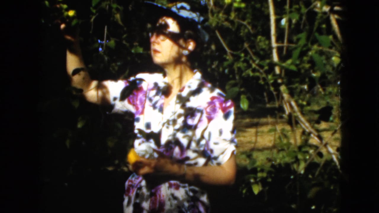 Woman in a floral dress stands by tree foliage with fruit in her hands.