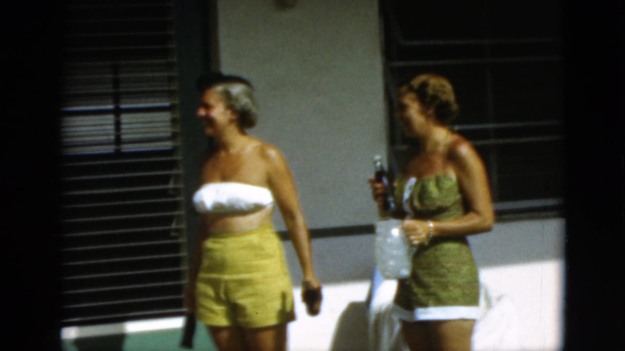 The two women remain on the Quebec patio, with one holding a bottle as they appear to talk in bright afternoon light.