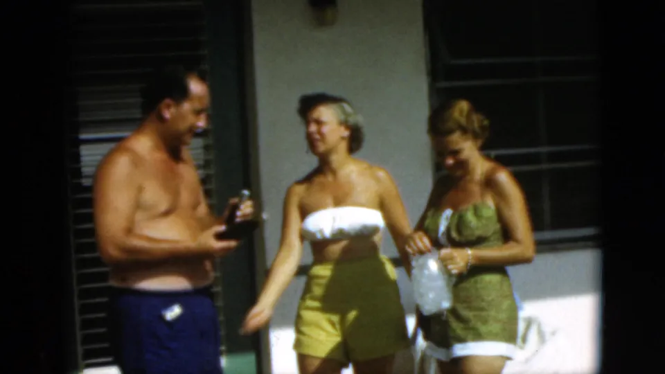 The man now holds the bottle as the two women stand nearby on the sunny Quebec patio, with chairs and shaded windows behind them.