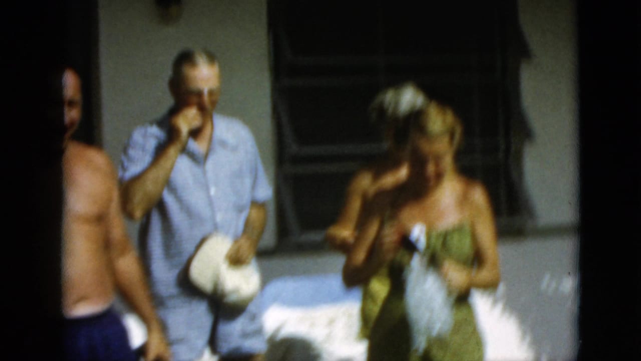 A man in a light blue checked outfit drinks near a woman in green swimwear during the Quebec summer gathering.