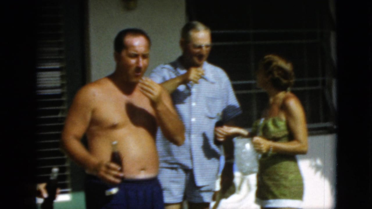 1952 Quebec home-movie frame showing a shirtless man with a beer bottle beside adults on a sunlit patio.