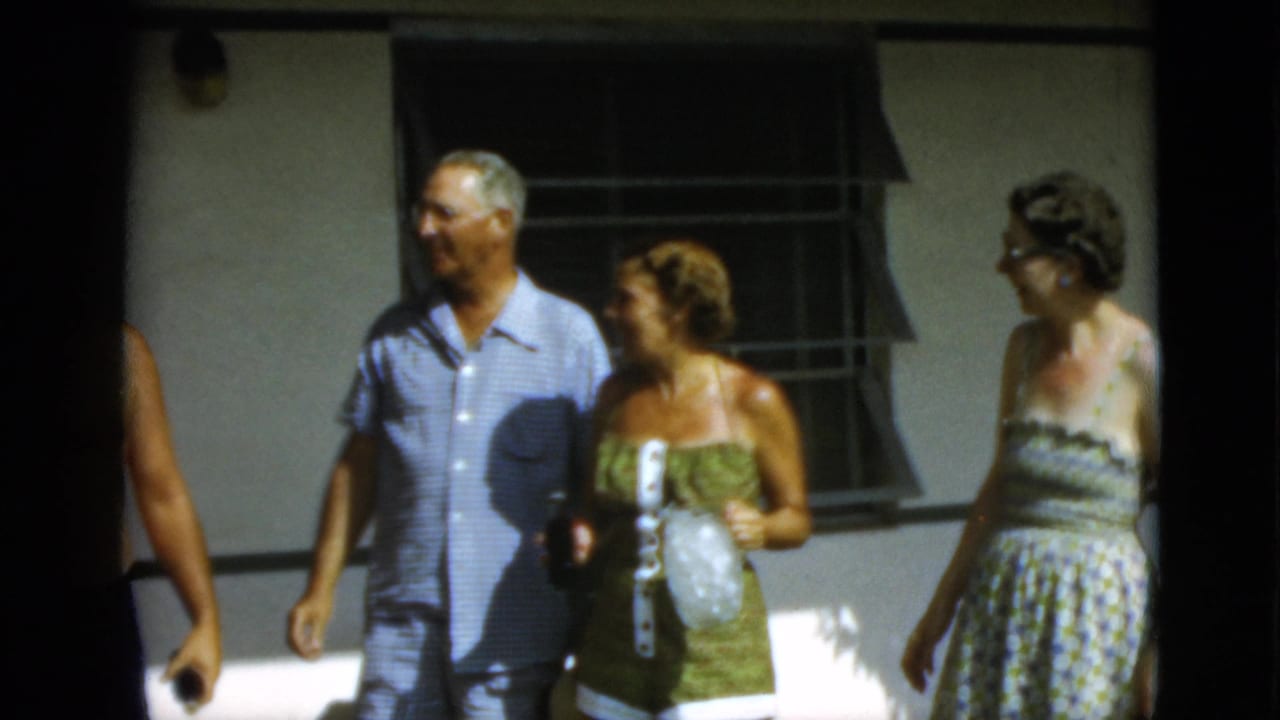 1952 Quebec frame with a man in a light blue short-sleeve shirt and two women walking and talking outdoors.