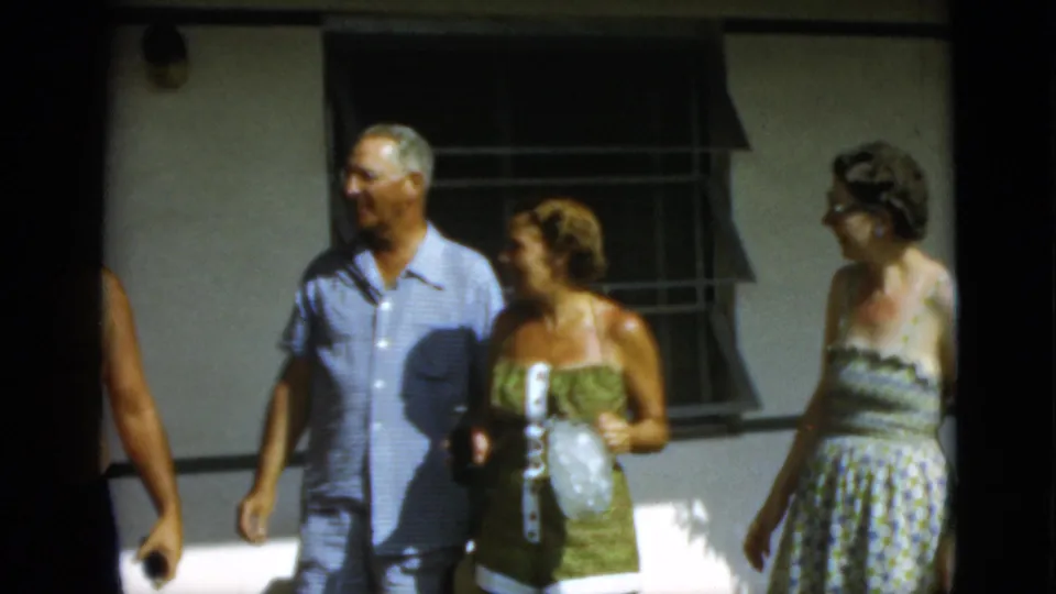 1952 Quebec frame with a man in a light blue short-sleeve shirt and two women walking and talking outdoors.