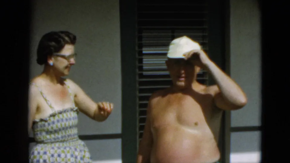 The woman gestures casually while the man raises his hand to adjust his white cap in this 1952 Quebec outdoor home-movie frame.