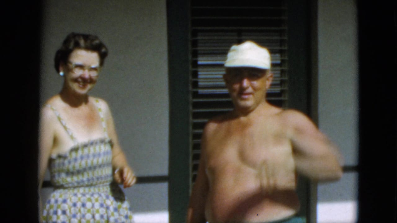 In 1952 Quebec home-movie footage, a woman in glasses and a patterned dress smiles beside a shirtless man wearing a white cap.