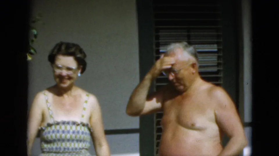 A woman in glasses smiles as a shirtless older man wipes his forehead, suggesting a hot summer moment in Quebec in 1952.