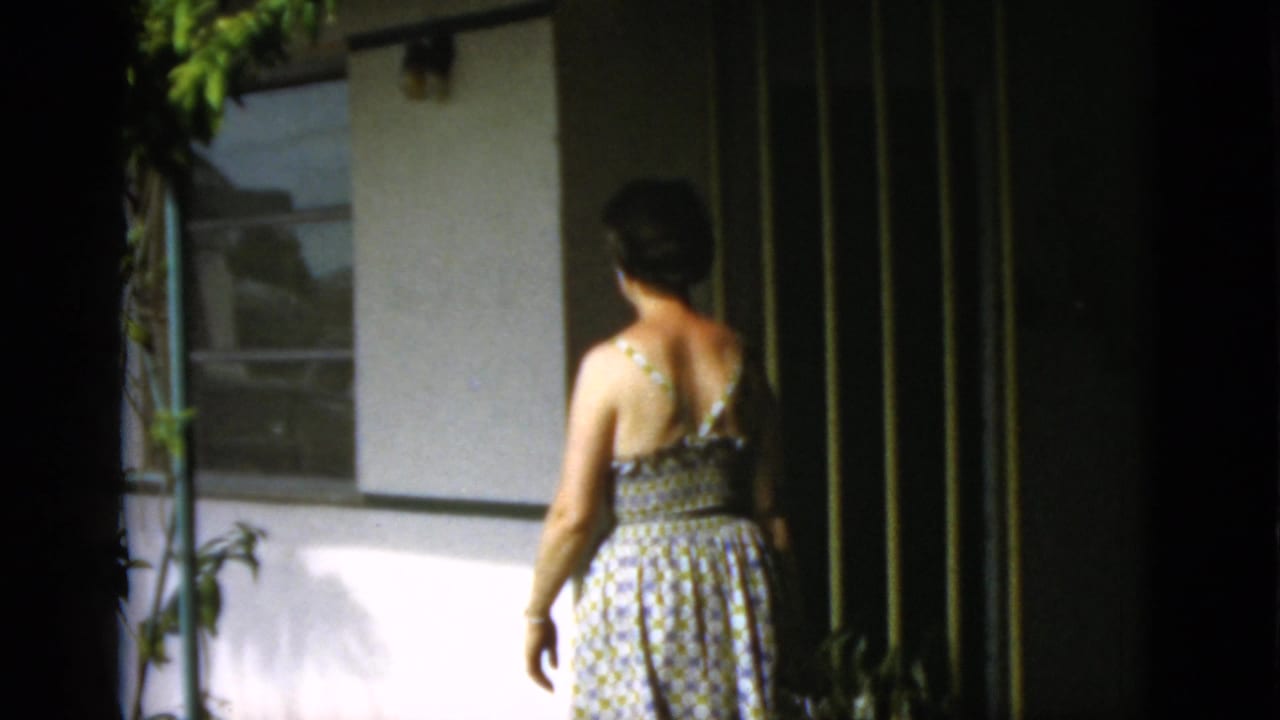 Woman in a patterned sundress walking toward a low building.