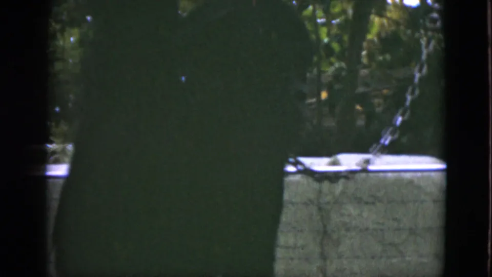 A dark, partially obscured ape figure stands near a low wall and chain in the 1952 Quebec zoo footage.