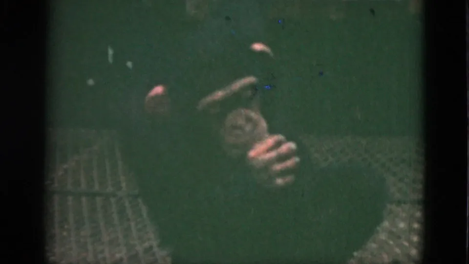 1952 Quebec home-movie frame of a chimpanzee on a grate floor, hand raised near the mouth in the enclosure.