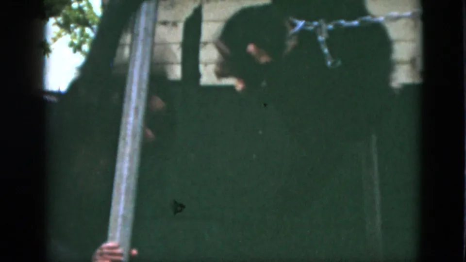 1952 Quebec frame with the chained primate seated in shadow beside cage bars and a pale wall edge.