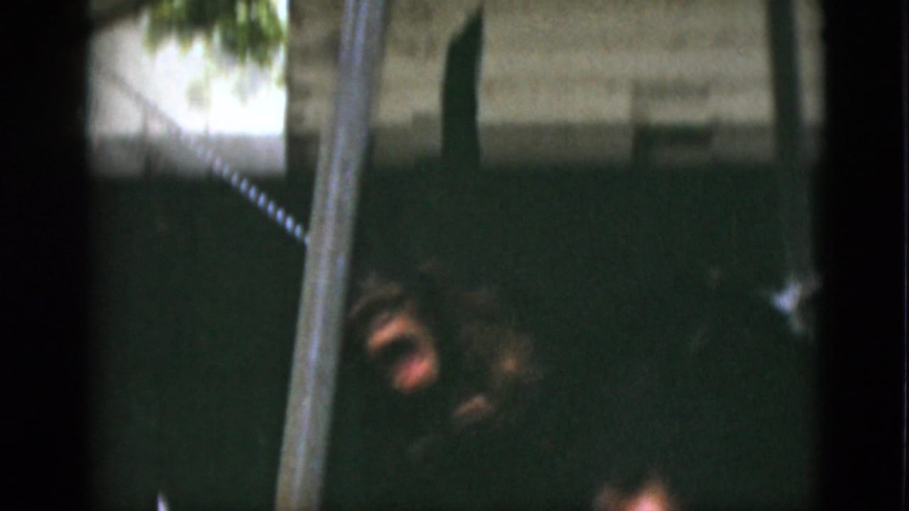 1952 Quebec 8mm frame showing a chimpanzee low in a dark enclosure near a vertical pole and visible chain restraint.