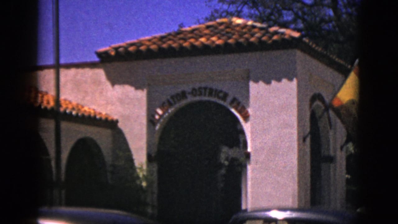 1952 Quebec home-movie frame showing a white stucco Alligator-Ostrich Farm entrance with an arched opening and terracotta roof.