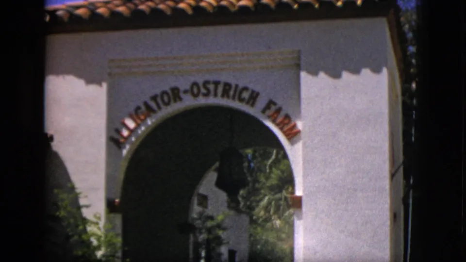1952 Quebec frame showing the Alligator-Ostrich Farm gateway from outside, with a bell hanging inside the arch.