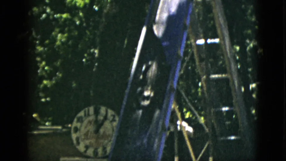 8mm home movie circa 1952, Quebec: wooden slide structure in close-up with a round analog clock in the lower-left corner and a dark animal shape on the slide.