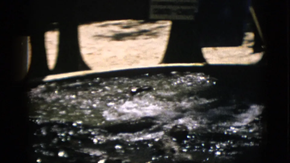 8mm film frame circa 1952, Quebec: water pool with turbulent splash and dark animal shape entering; structural enclosure wall and possible signage in background.