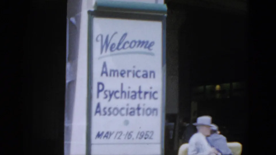 8mm color frame from a 1952 Quebec convention venue: APA welcome banner on pillar, hat-wearing attendee seated in yellow upholstered chair at right.
