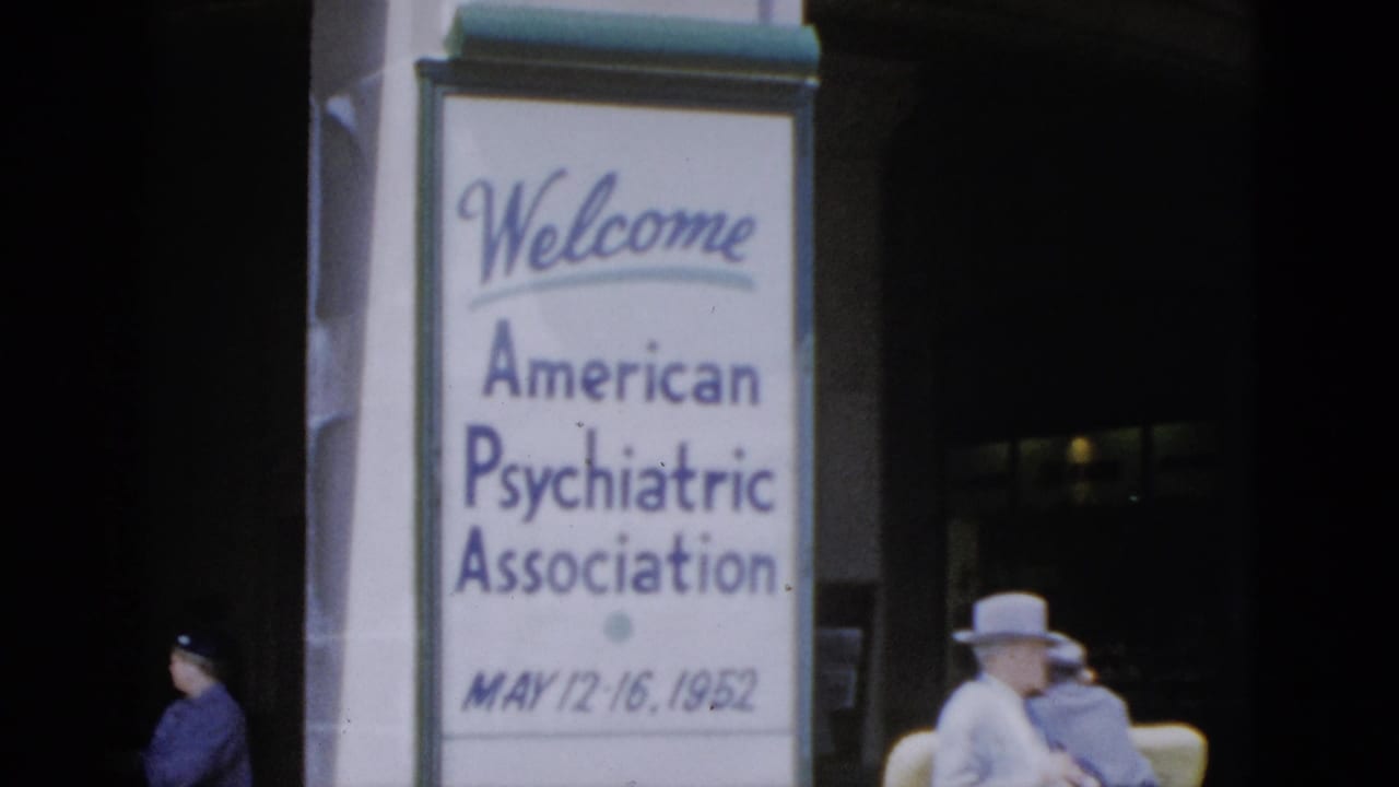 APA welcome sign on pillar; hat-wearing figure seated at right, second figure in dark clothing passing through background.