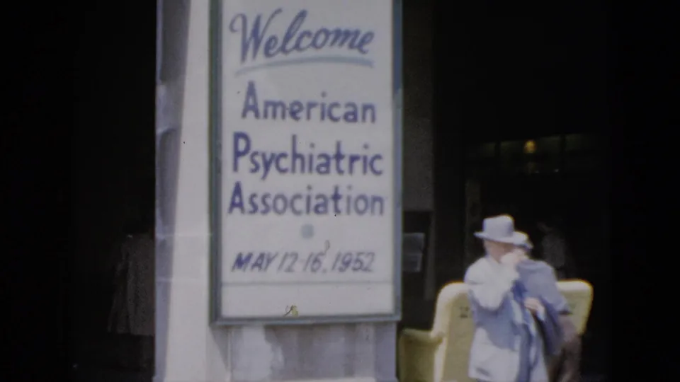 Final 8mm frame from 1952 Quebec APA conference footage; welcome sign centered on pillar, the hat-wearing figure at right has shifted posture in the yellow chair.