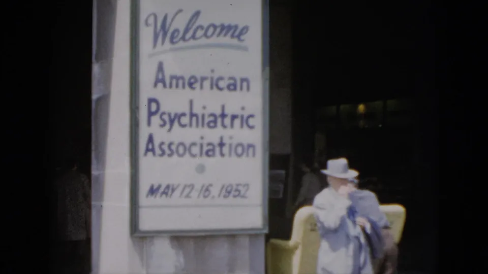 8mm color footage, Quebec 1952: large conference welcome sign for the American Psychiatric Association (May 12-16) with a woman in white hat and blue dress at a building entrance.