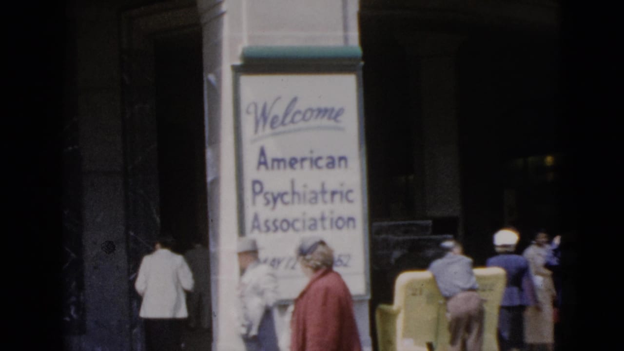 8mm color footage, Quebec 1952: APA conference welcome sign at a building entrance, with several attendees in period dress including a woman in a red jacket and a figure in white.