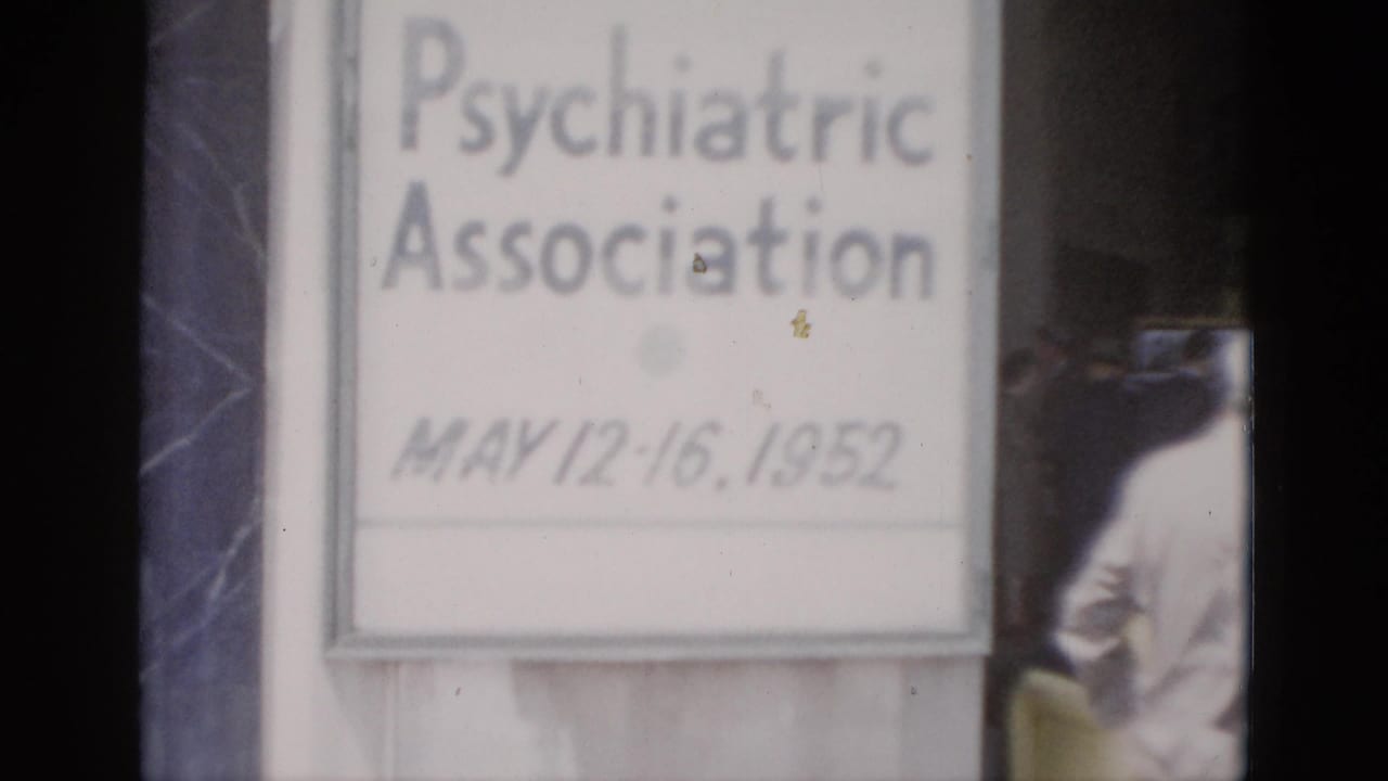 Close-up of conference welcome sign dated May 12–16, 1952, on 8mm color film; partial adult figure at right edge; film dust artifacts visible on sign surface.