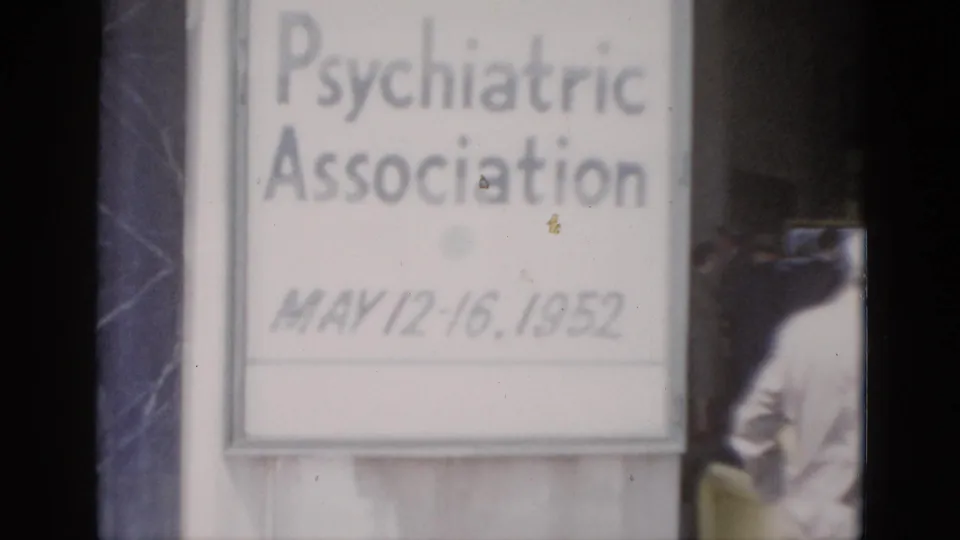 Close-up of conference welcome sign dated May 12–16, 1952, on 8mm color film; partial adult figure at right edge; film dust artifacts visible on sign surface.