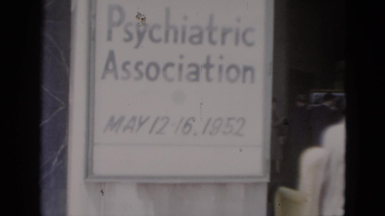 Repeated close-up of the May 1952 conference sign on 8mm color film; dark structural element now at frame left; film grain and dust spot visible near upper right of sign.