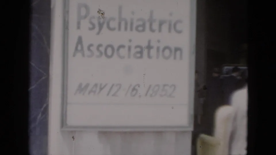 Repeated close-up of the May 1952 conference sign on 8mm color film; dark structural element now at frame left; film grain and dust spot visible near upper right of sign.