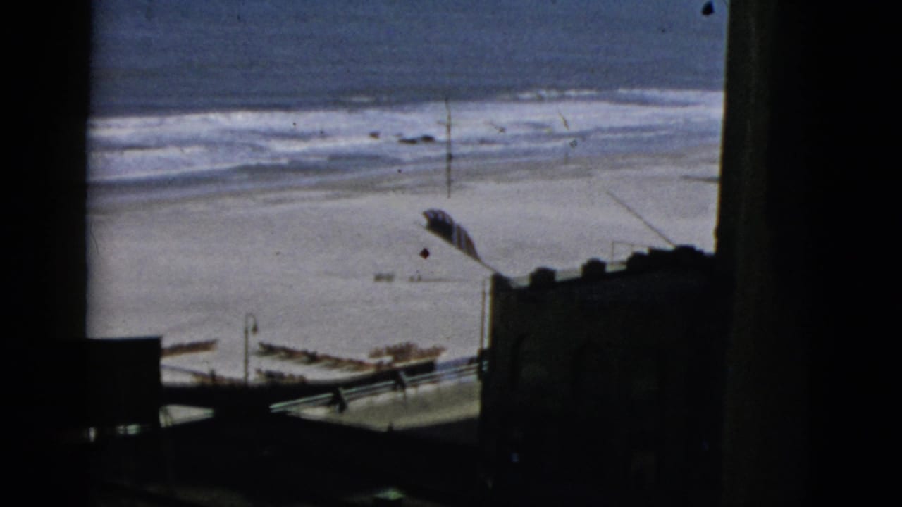 Elevated view of a sandy beach and breaking ocean waves, with dark wooden structure elements framing the lower foreground.