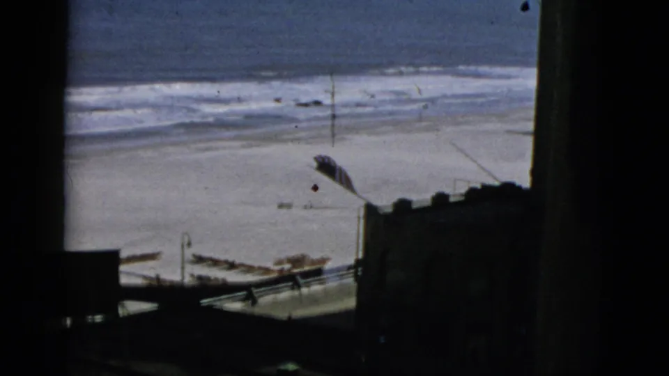 Elevated beach overlook showing surf and sand, framed by dark wooden foreground elements, 8mm home movie, stated Quebec, Canada, 1952.