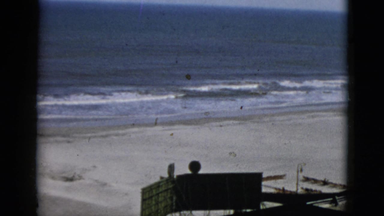 Beach and ocean from an elevated boardwalk vantage, dark booth structure at lower right, 8mm, stated Quebec, Canada, 1952.